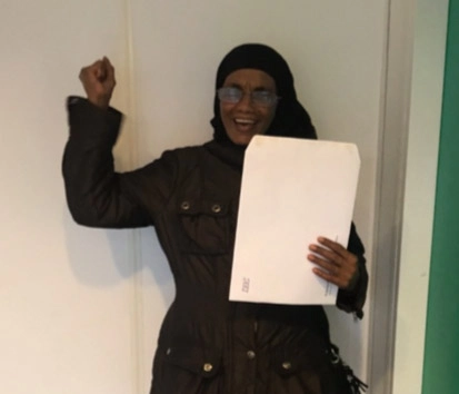 Invandrekvinde har et stykke papir i den ene hånd og løfter den anden hånd knyttet i vejret